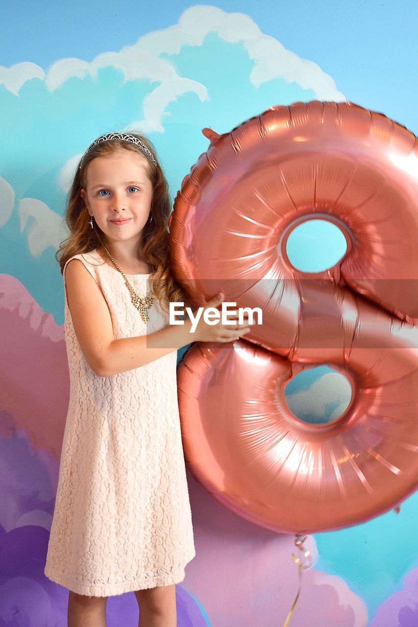 Portrait of girl holding number 8 inflatable ring against mural