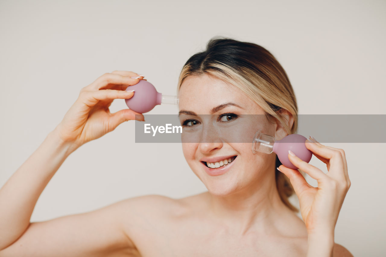 Portrait of smiling woman holding vacuum cup against colored background