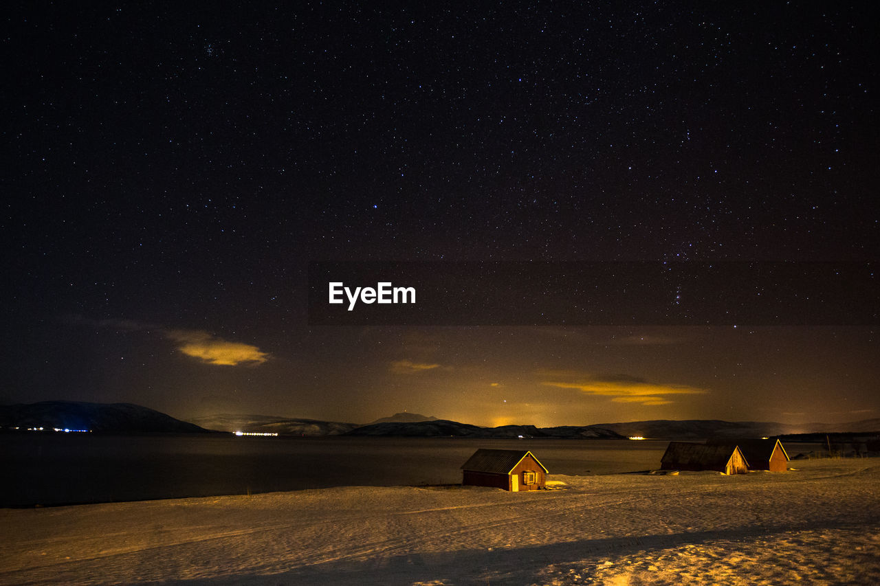 Houses on snow covered lakeshore against star field