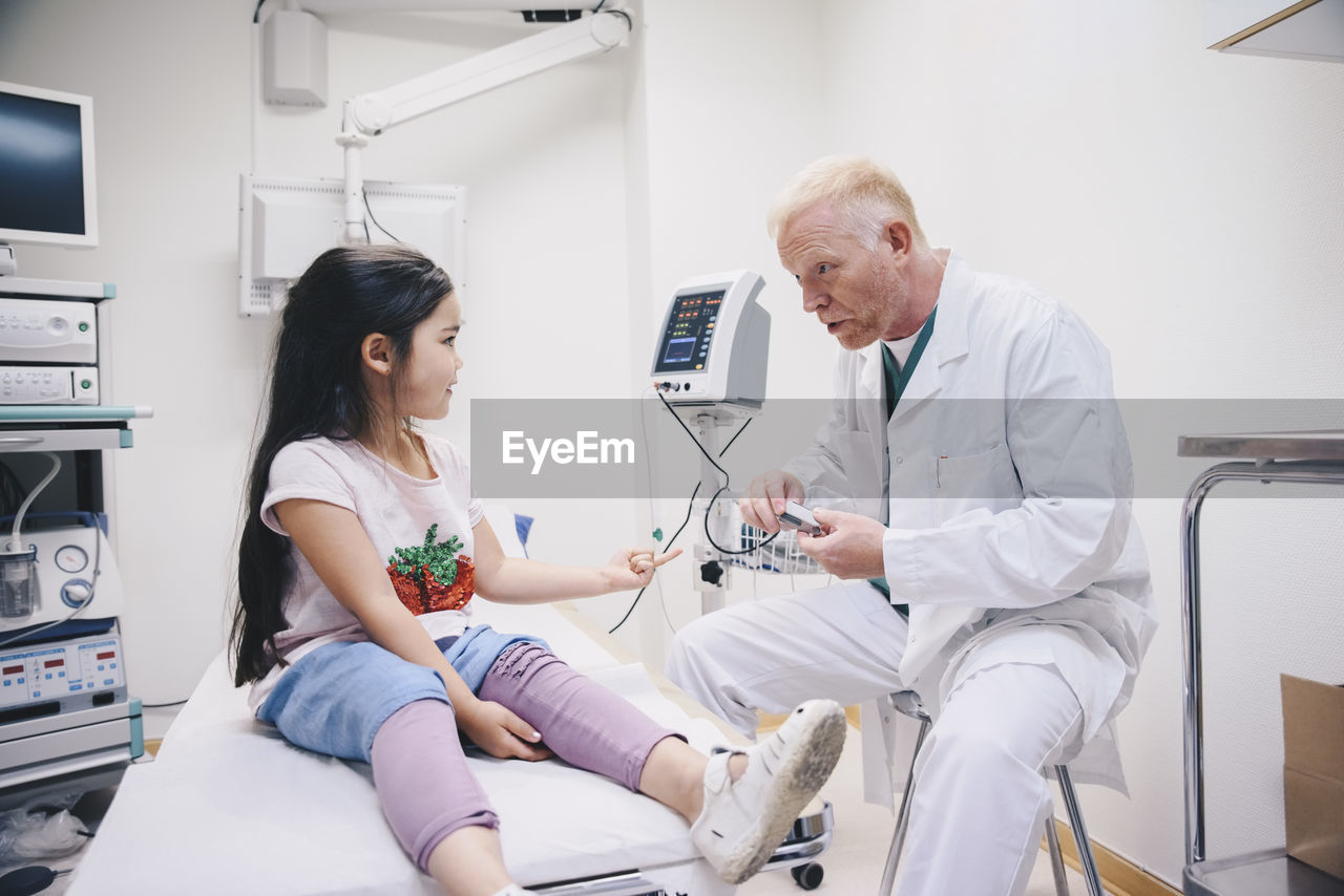 Mature doctor talking with girl while preparing pulse oxymeter at hospital