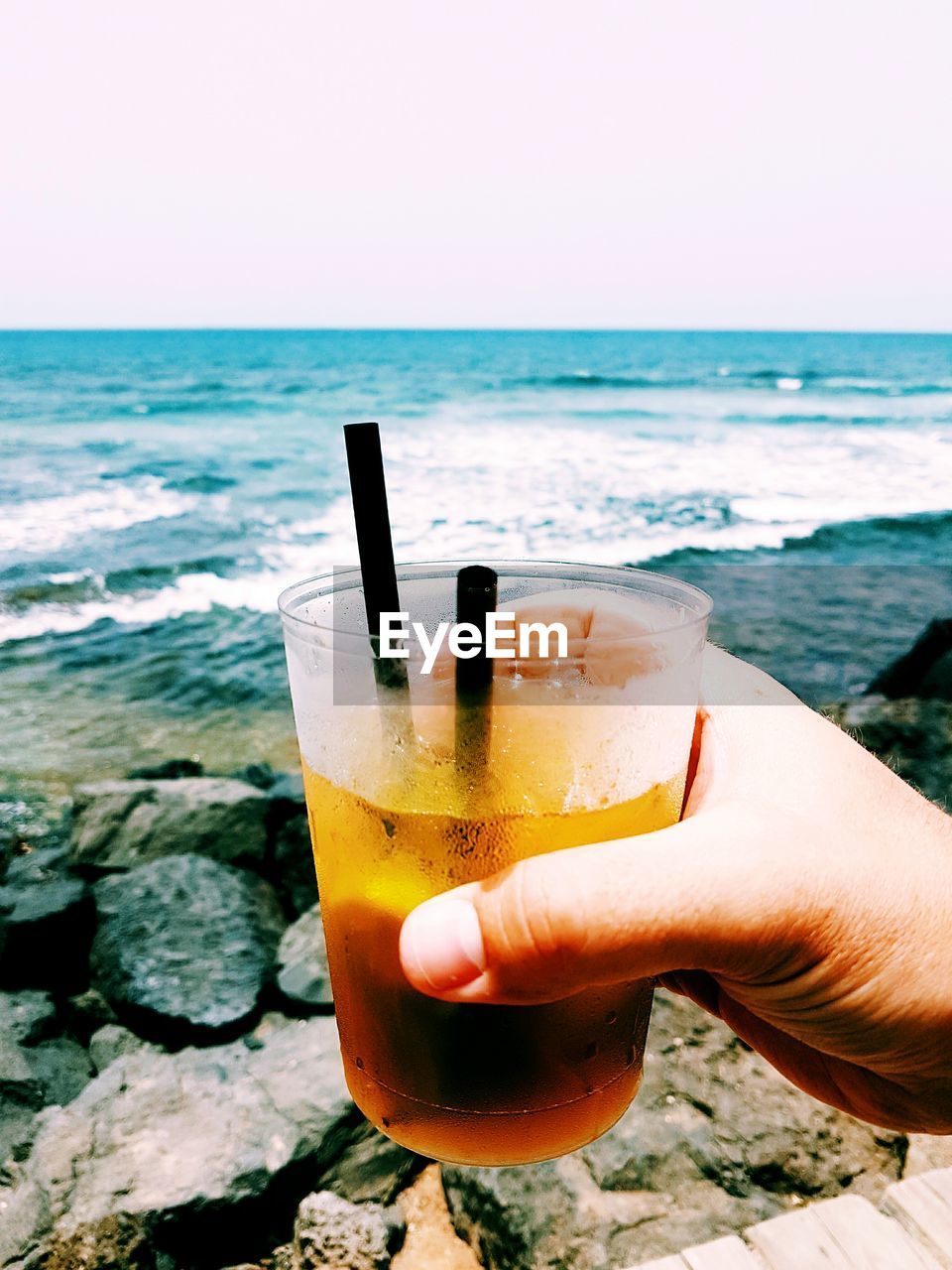 Cropped hand holding alcohol in glass at beach against sky