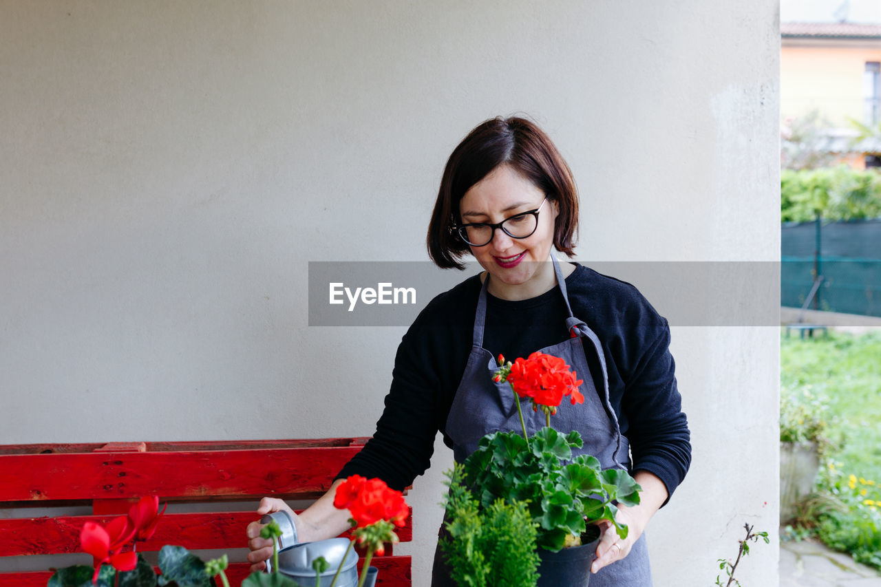 Dark haired woman standing with geranium flower pot in her hands