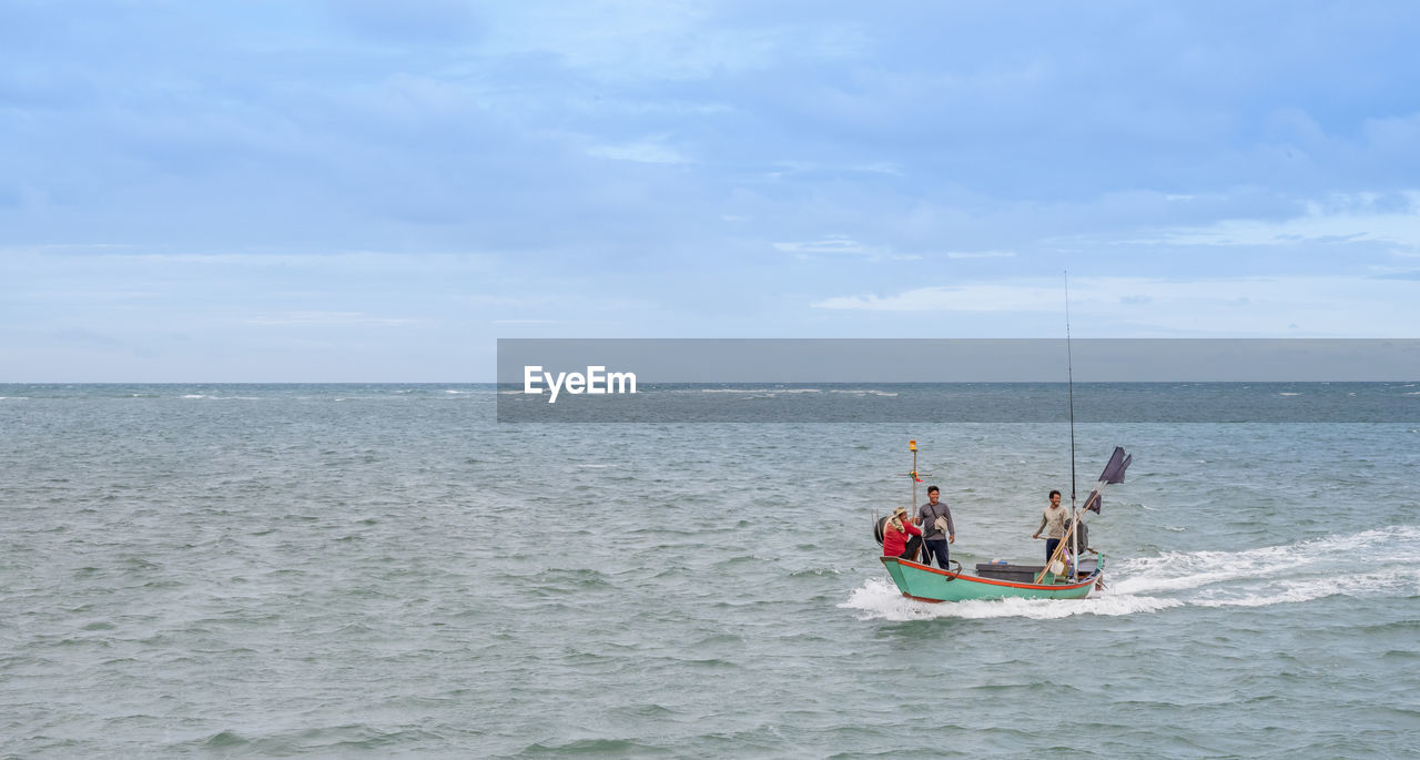 MEN ON BOAT IN SEA AGAINST SKY