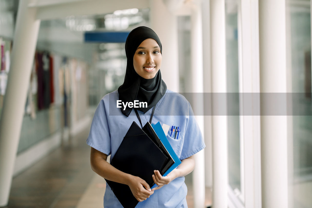 Portrait of smiling female nurse with file in hospital corridor