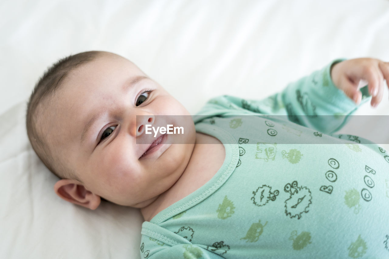 Close-up portrait of smiling toddler lying on bed at home