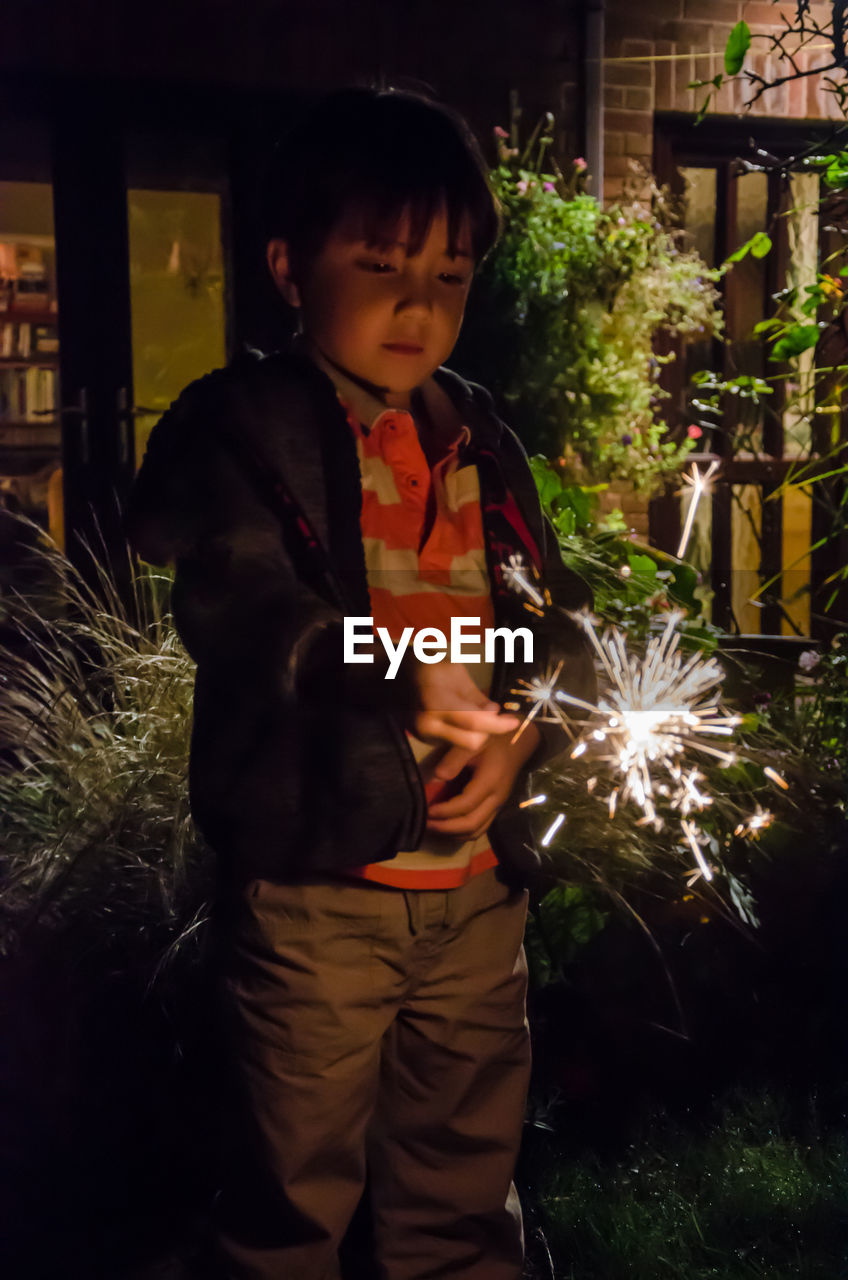 Boy holding sparkler while standing at night