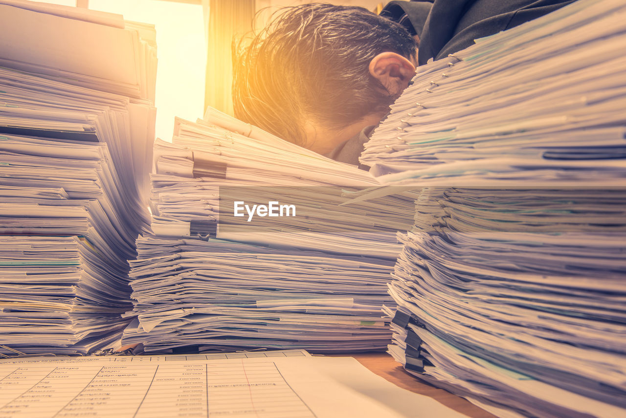 Tired businessman on stacked papers at desk in office
