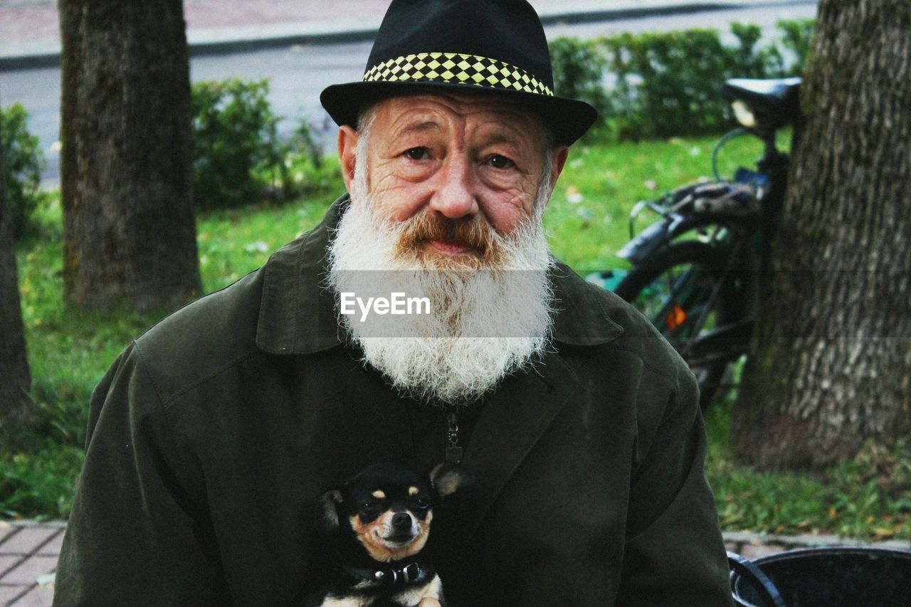 Portrait of mature bearded man with dog sitting in park