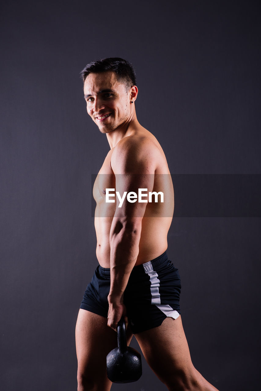 portrait of shirtless young man exercising against black background