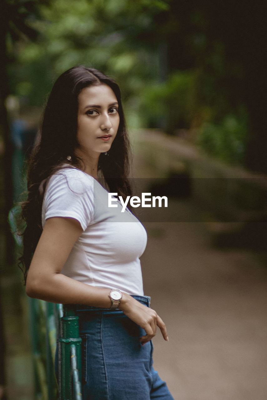 Portrait of smiling woman standing by railing against tree