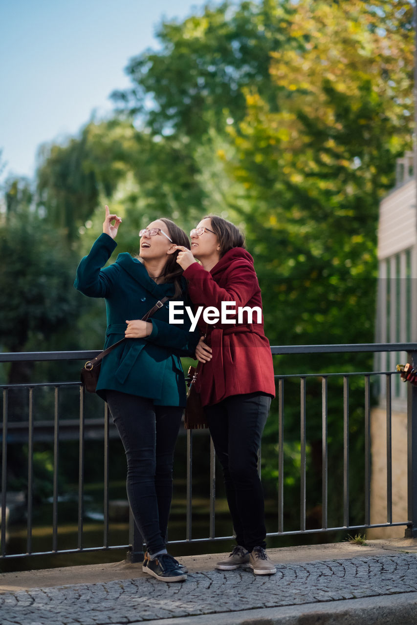 Sisters pointing while standing by railing in city