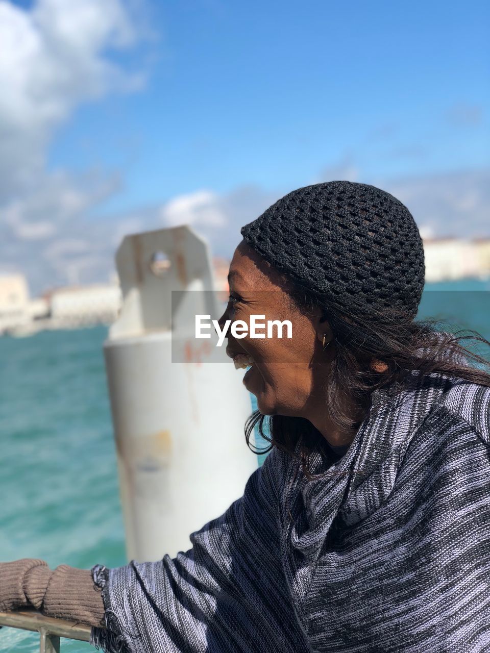 Smiling woman wearing knit hat by sea against sky