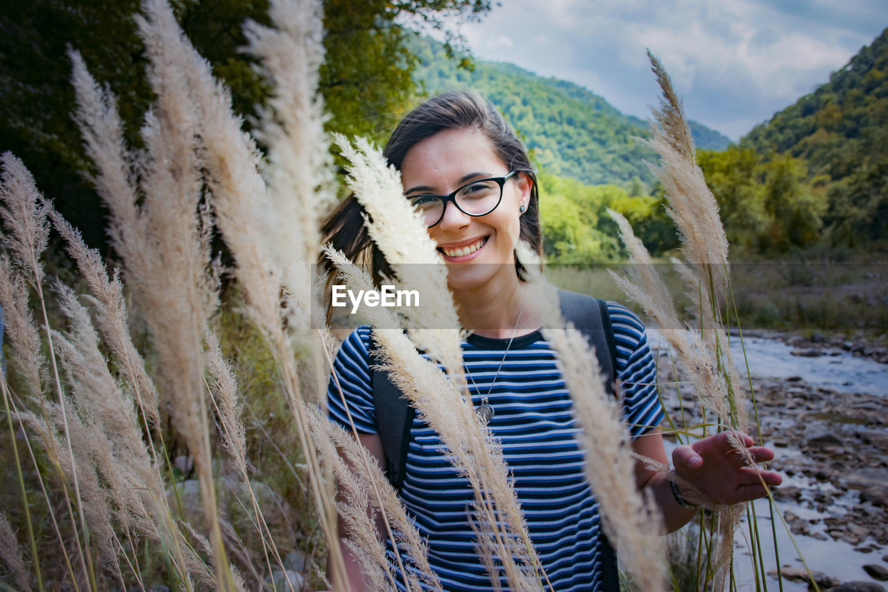 PORTRAIT OF HAPPY WOMAN STANDING AGAINST PLANTS