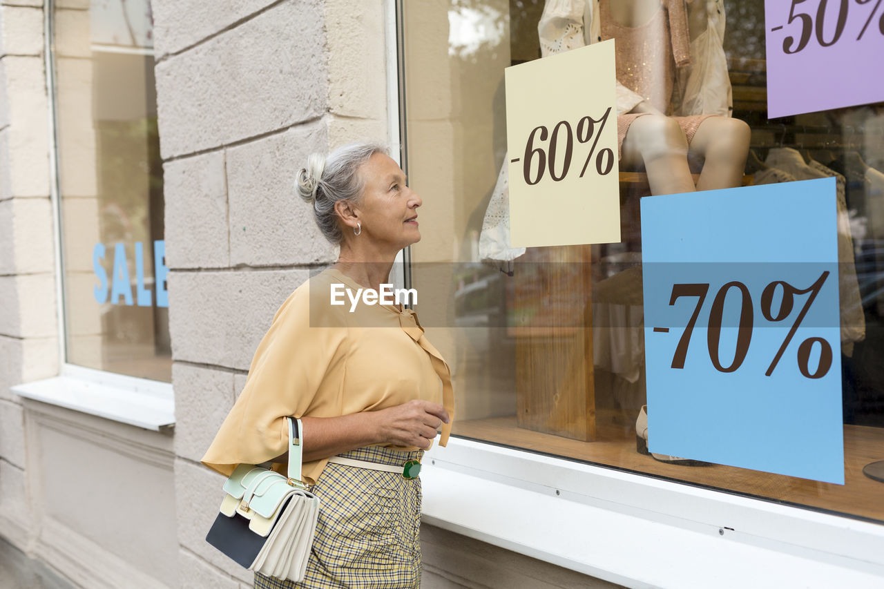 Smiling senior woman looking in shop window of a boutique