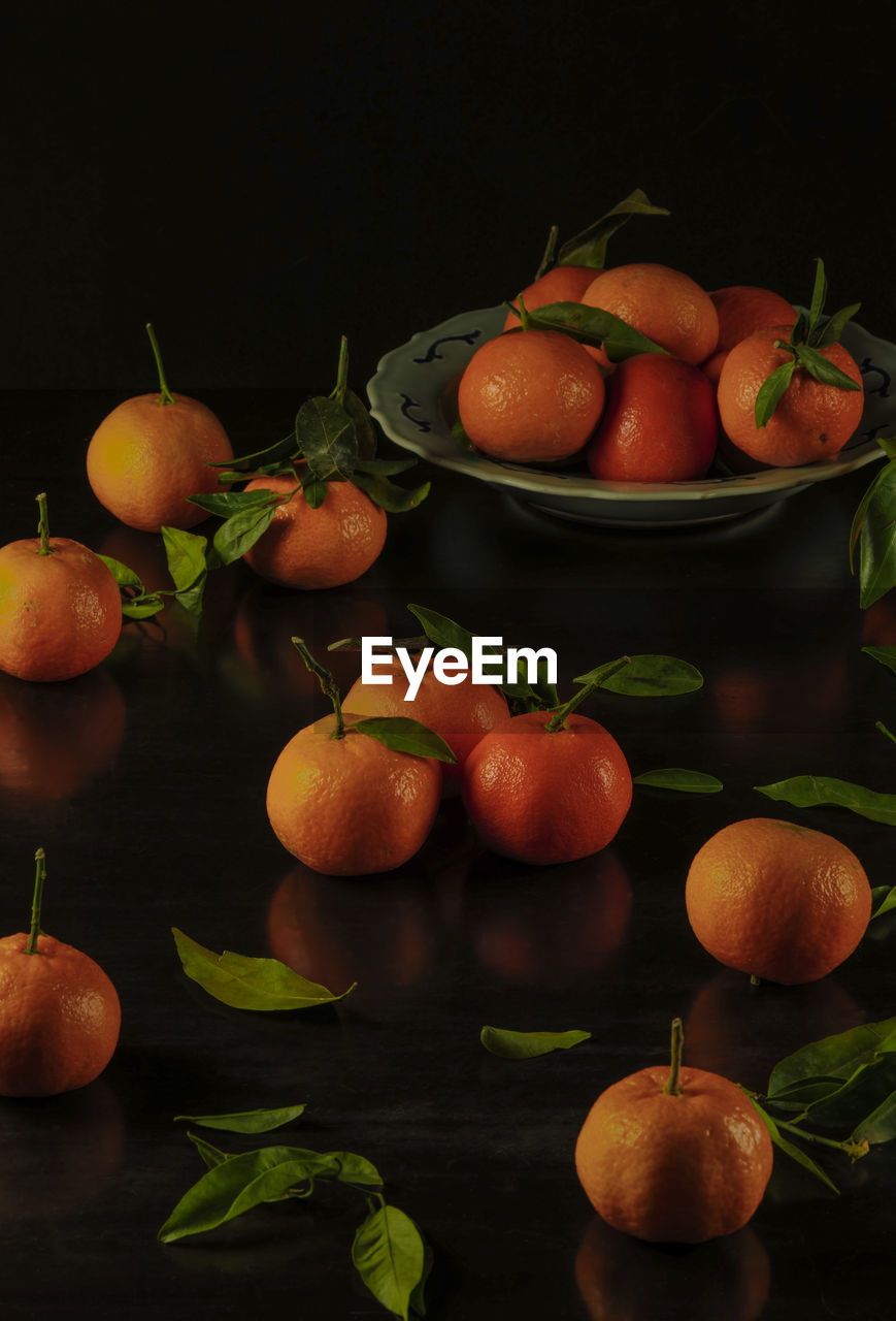 Still life of mandarins and leaves against black background