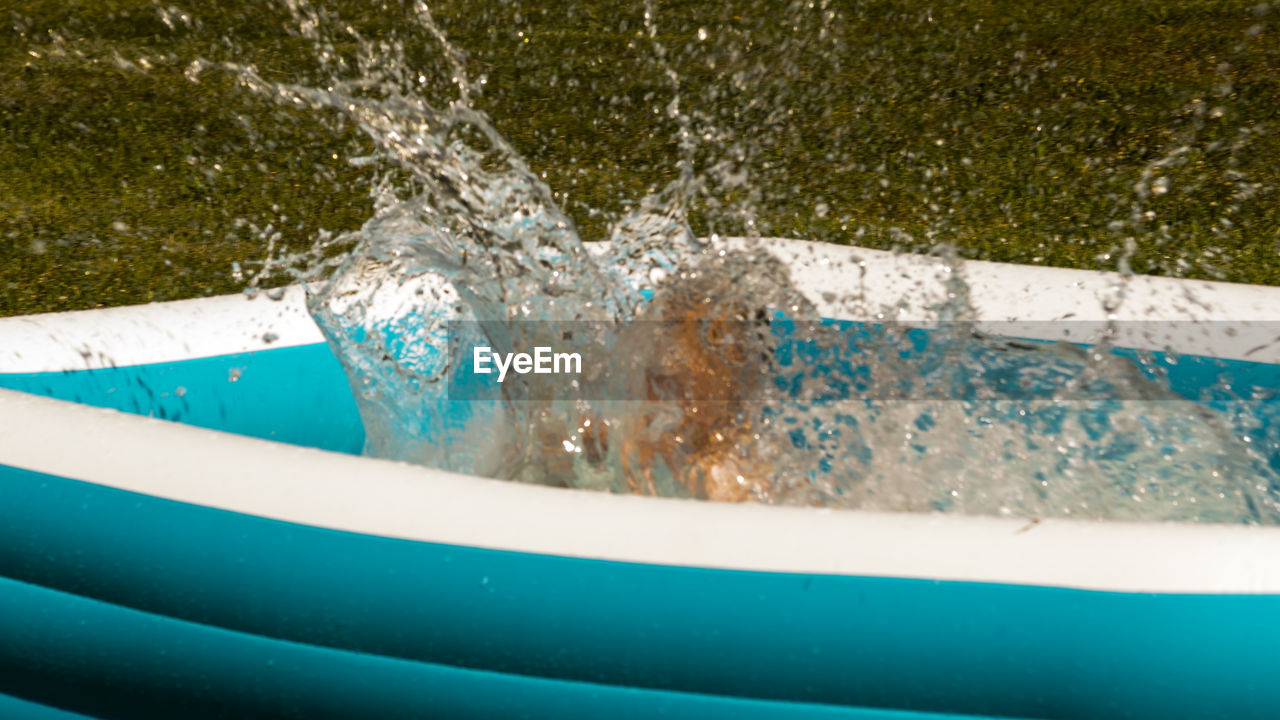 Child splashing water in inflatable swimming pool at yard