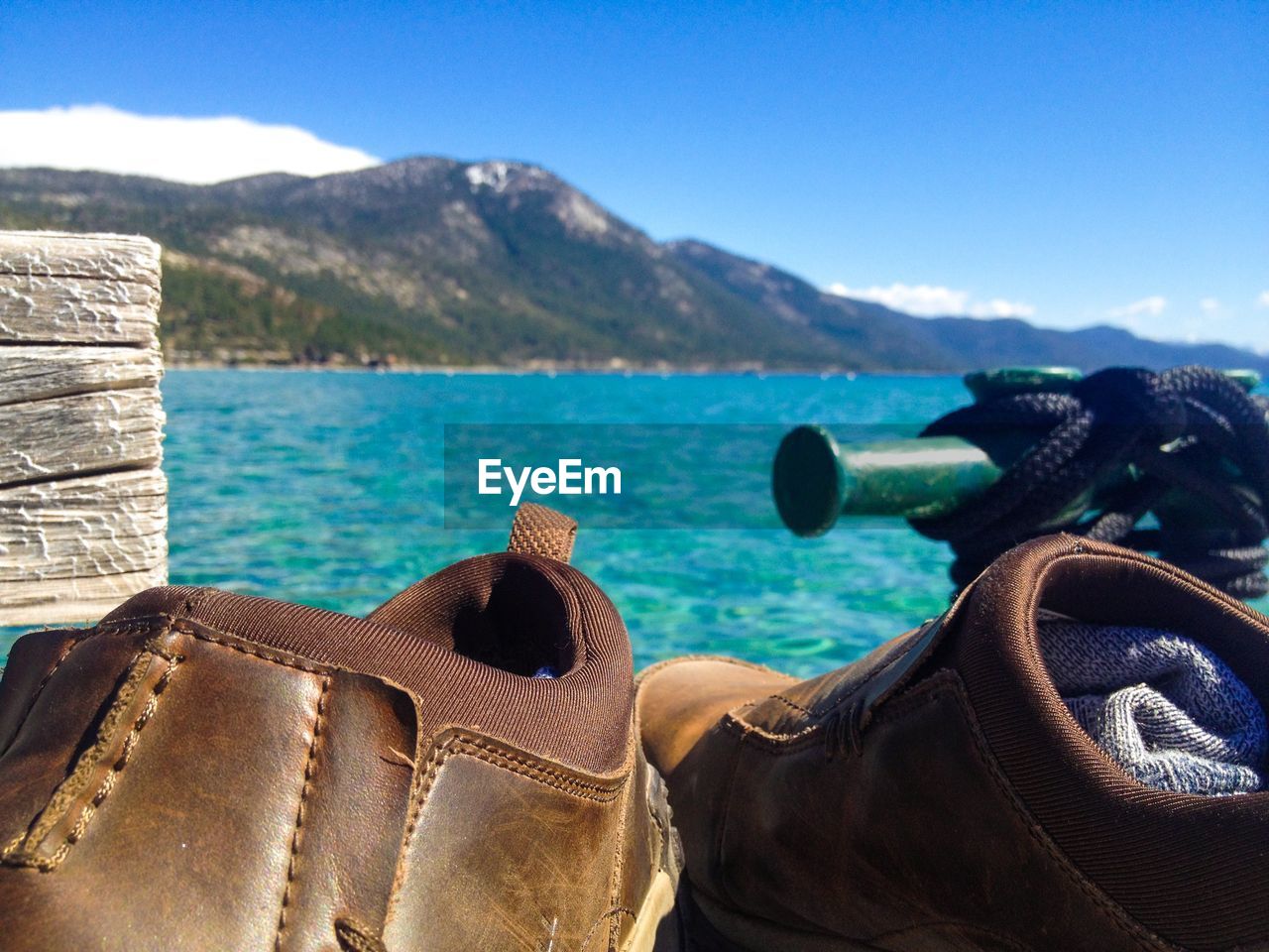 Close-up of shoes on pier against sea and mountain