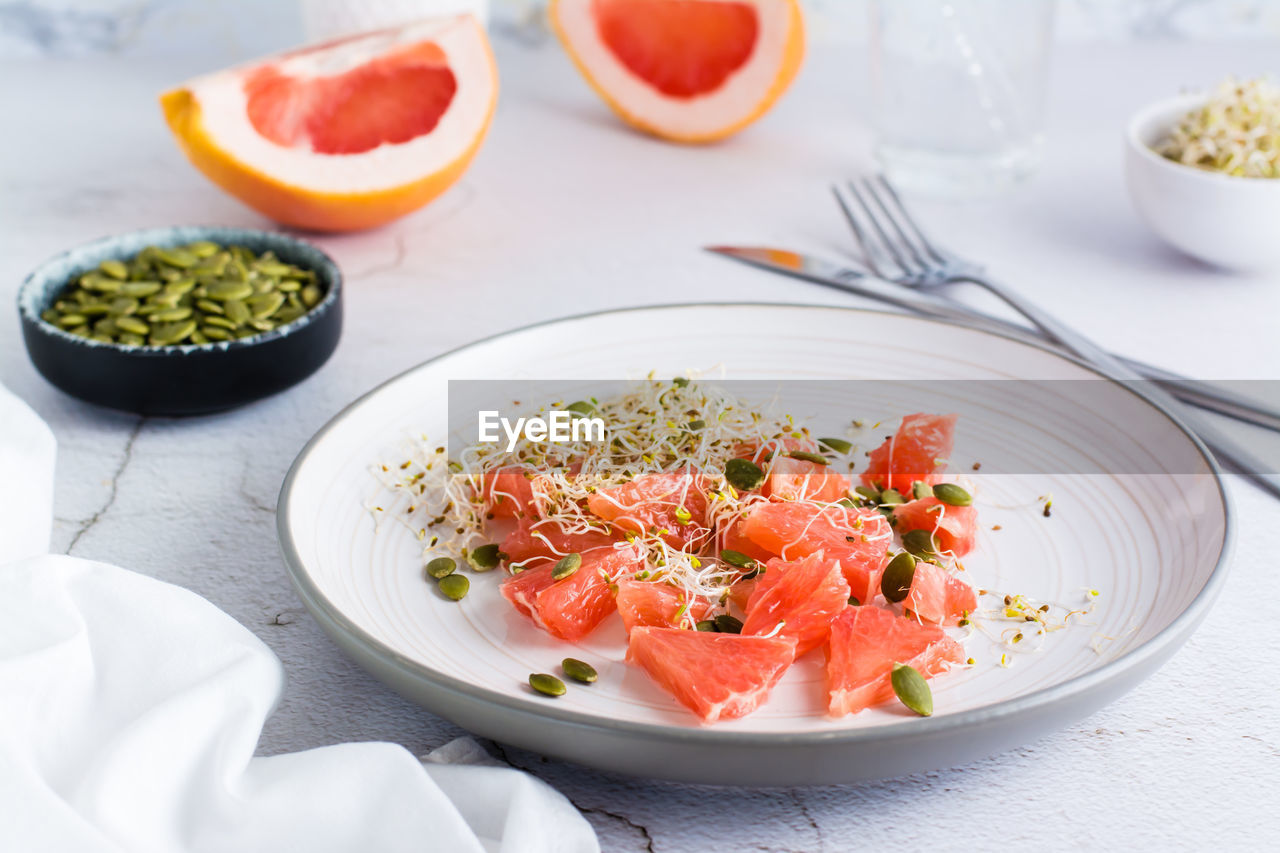 Fresh salad of grapefruit, clover and alfalfa sprouts and pumpkin seeds on a plate on the table. 