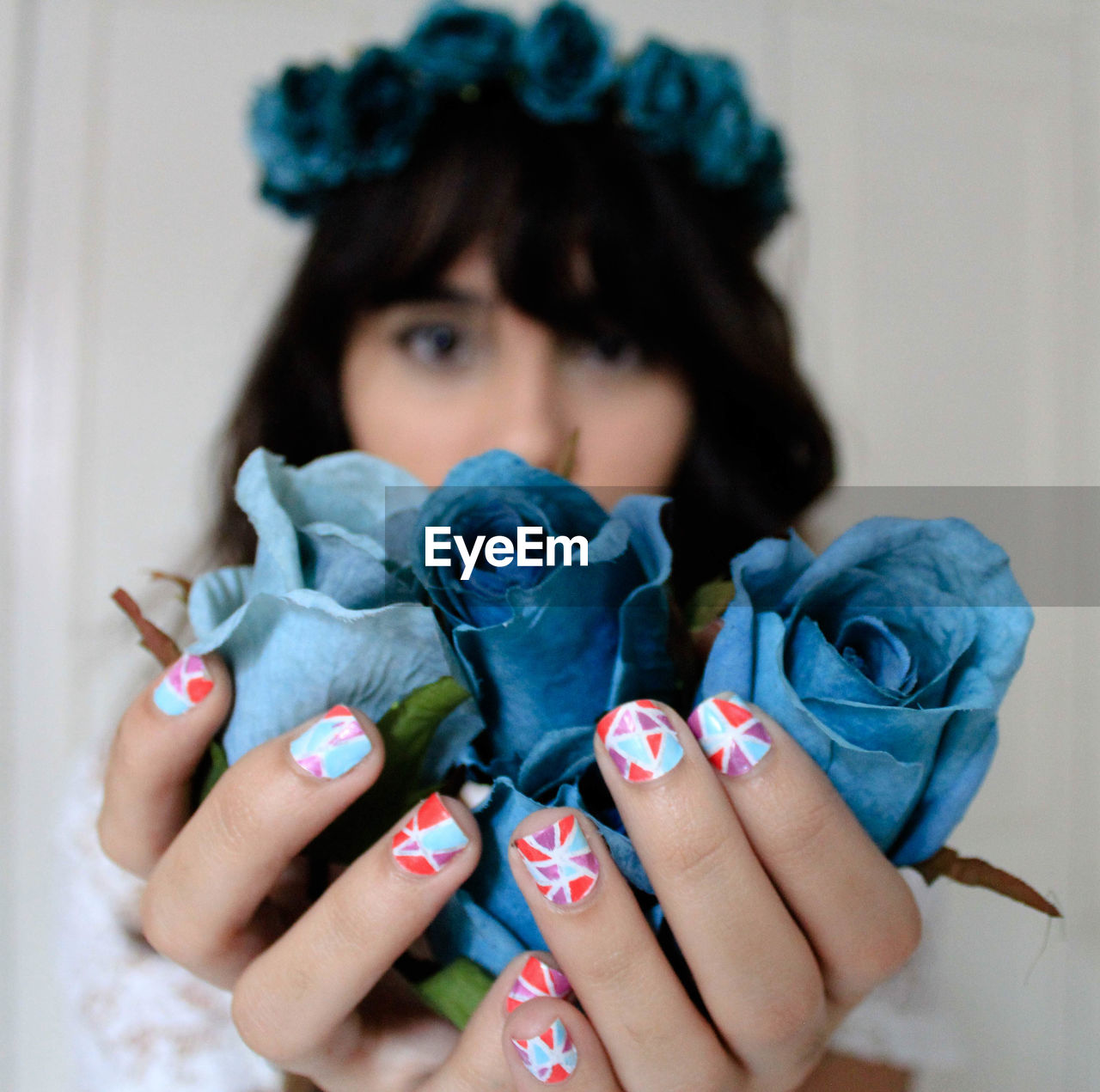 Woman with nail art holding artificial blue roses against wall