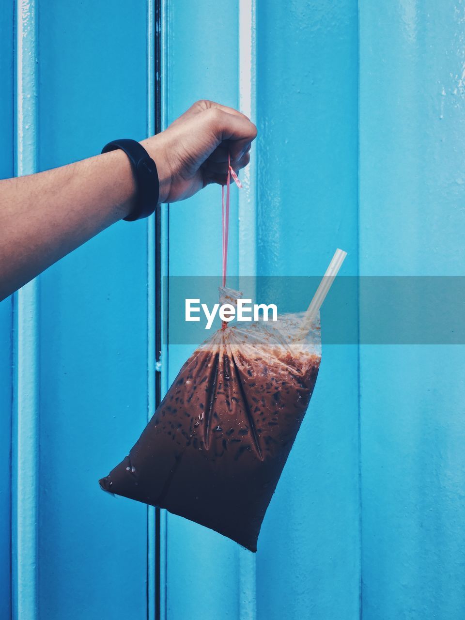 Cropped hand holding smoothie in plastic bag against wall