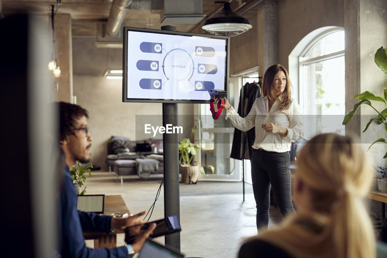 Confident businesswoman holding vr simulator while explaining during meeting