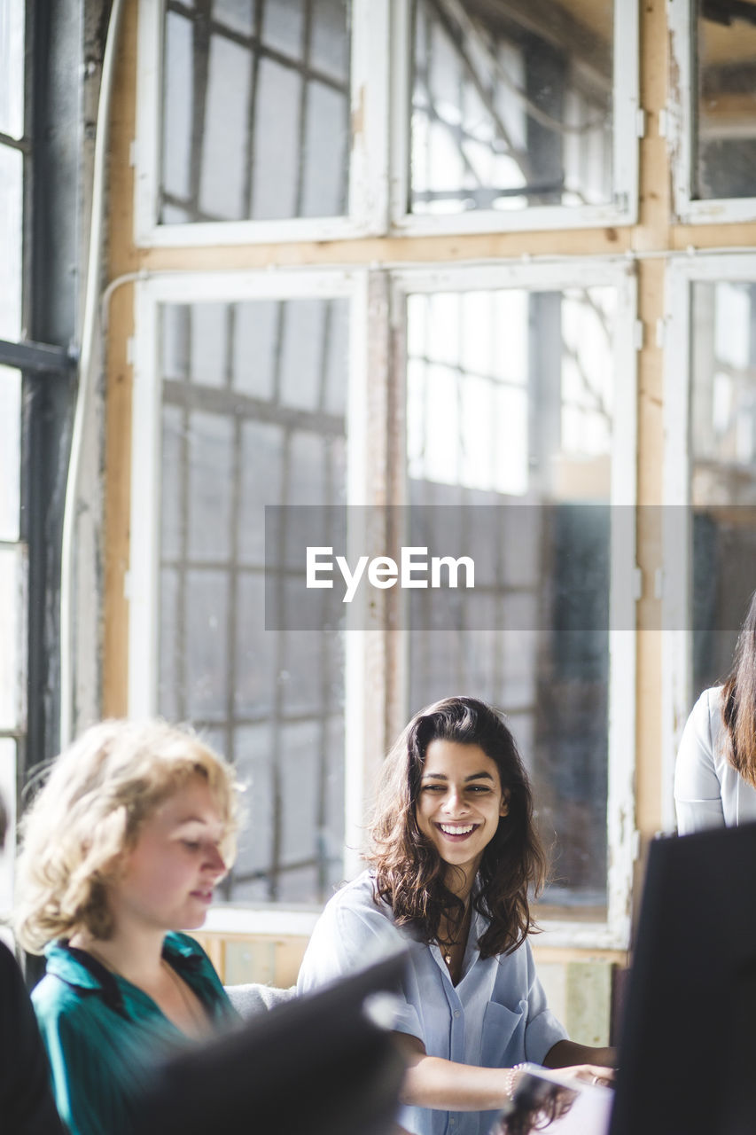 Smiling female computer programmer looking at coworker while working in creative office