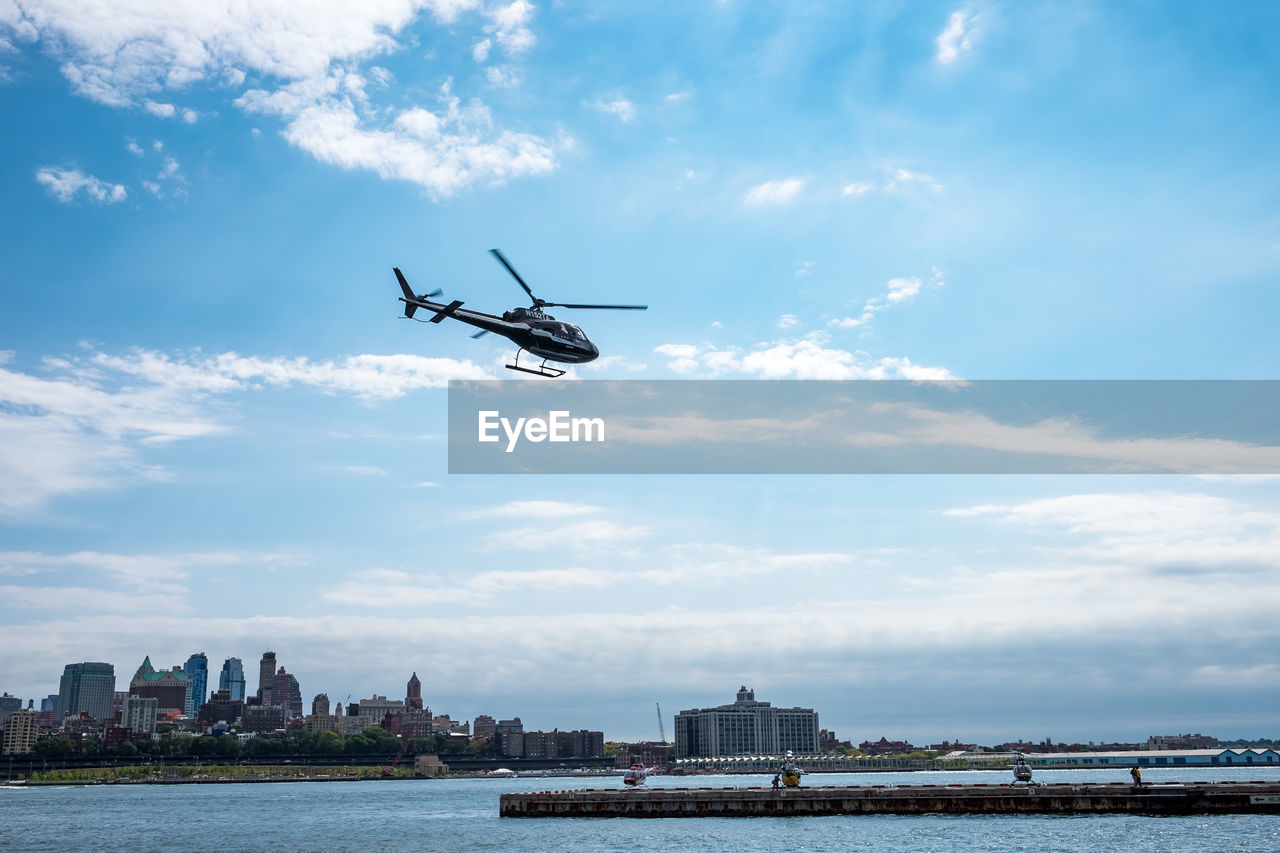 Low angle view of helicopter flying over lake against sky in city