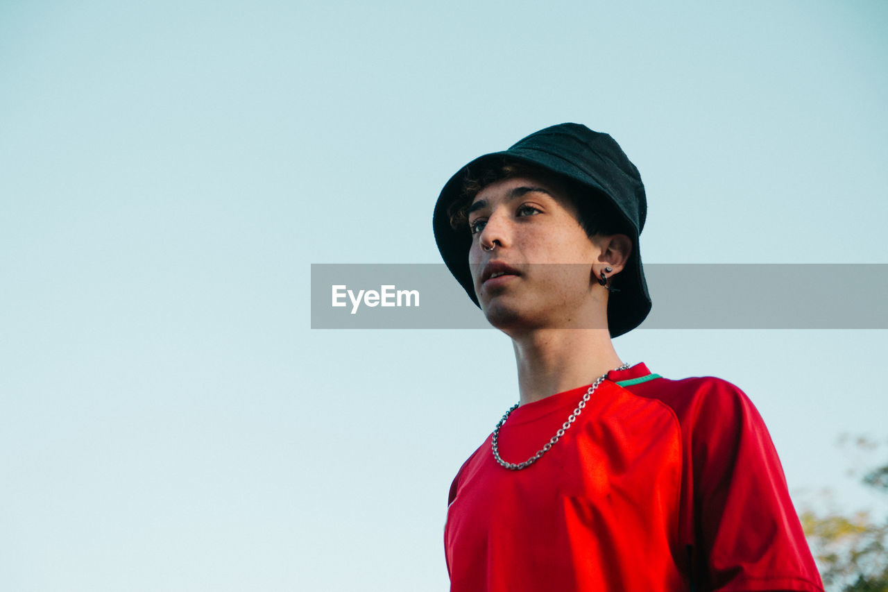 Portrait of young man looking away against clear sky