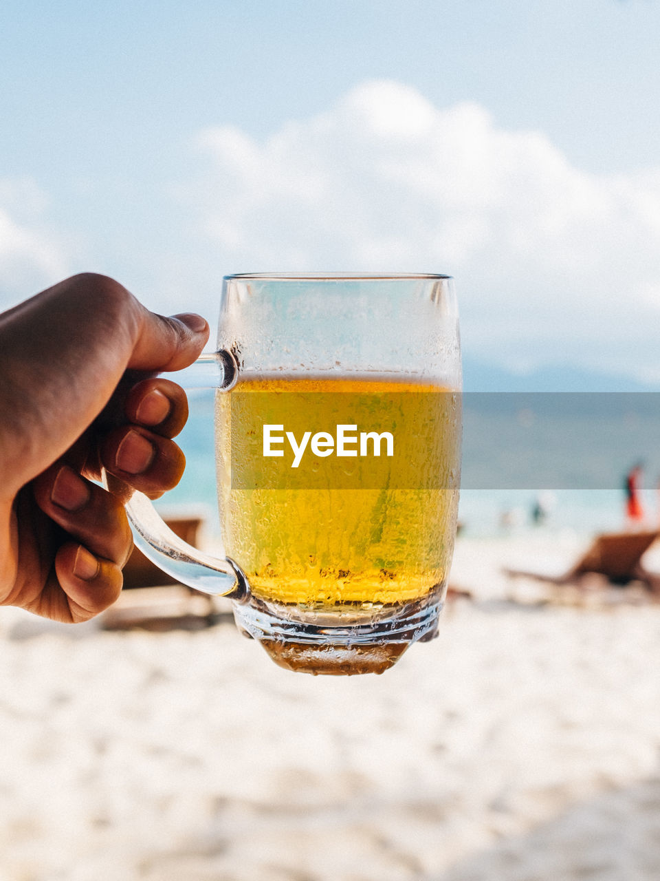 Cropped hand holding drinking glass at beach