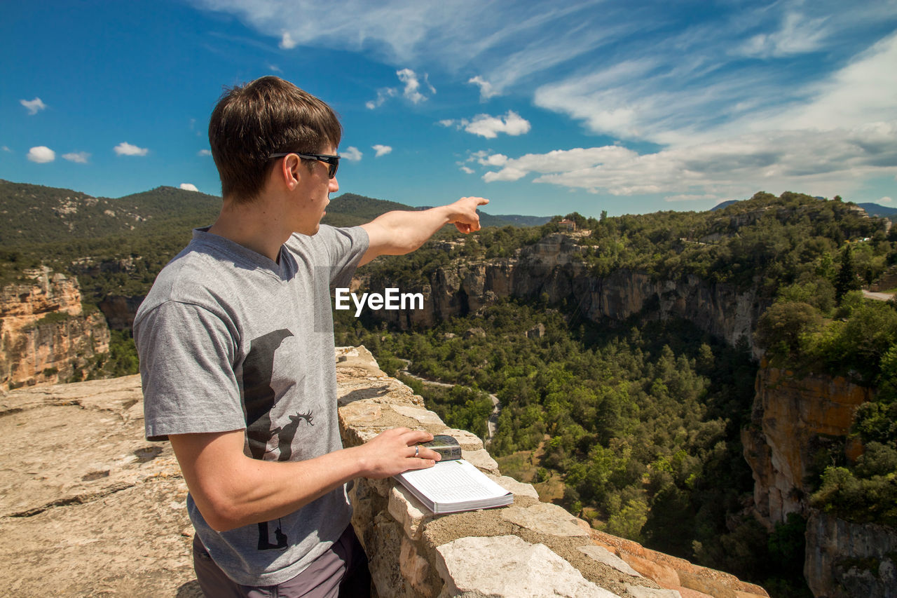 Young man pointing towards mountain during sunny day