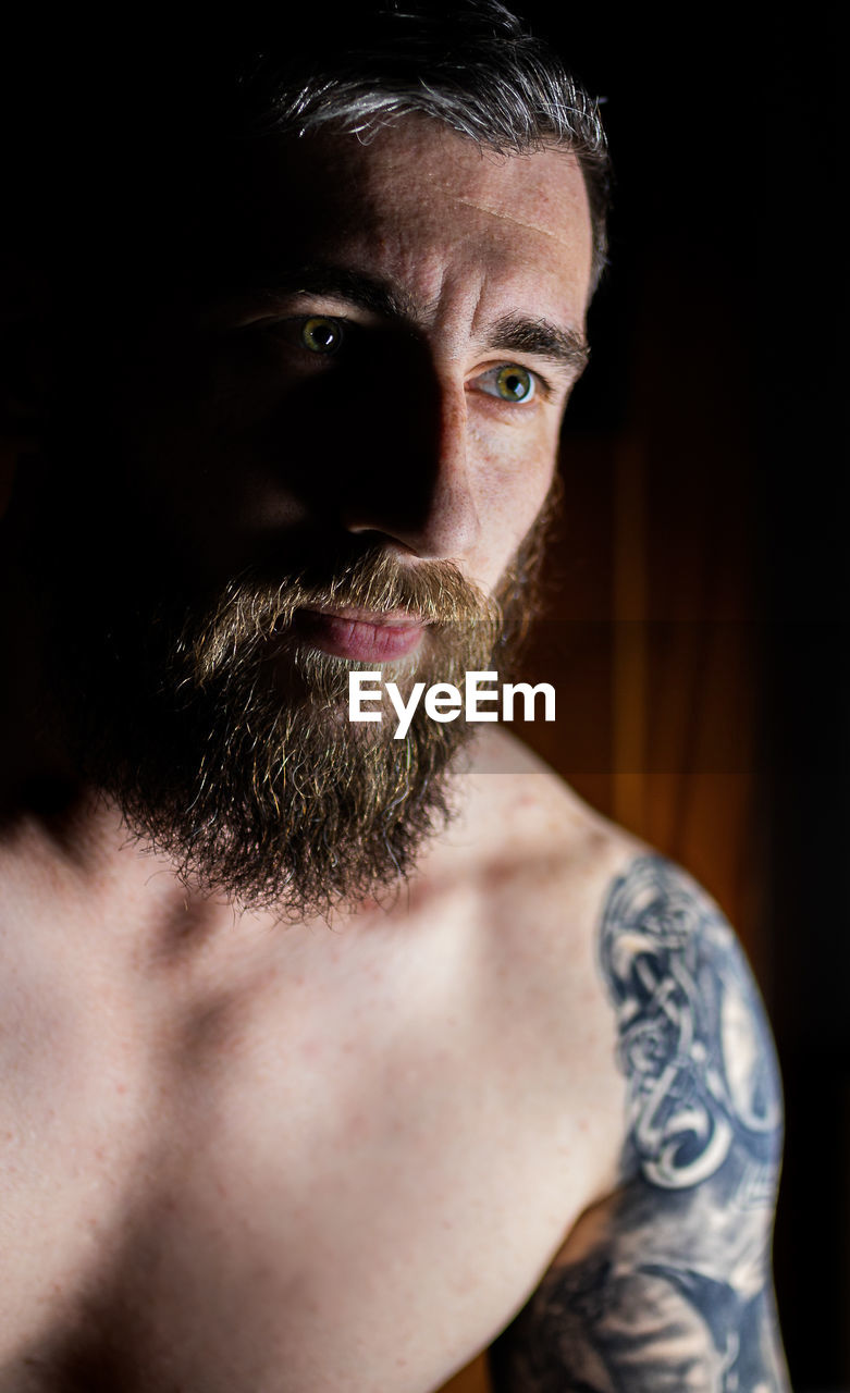 Close-up of shirtless man looking away in darkroom