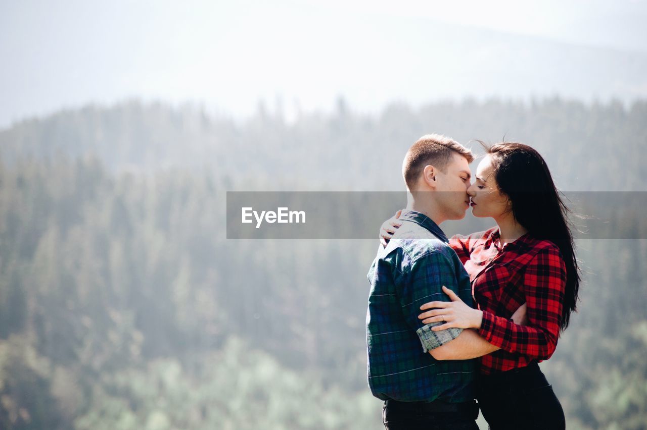 Side view of young couple kissing while standing in forest