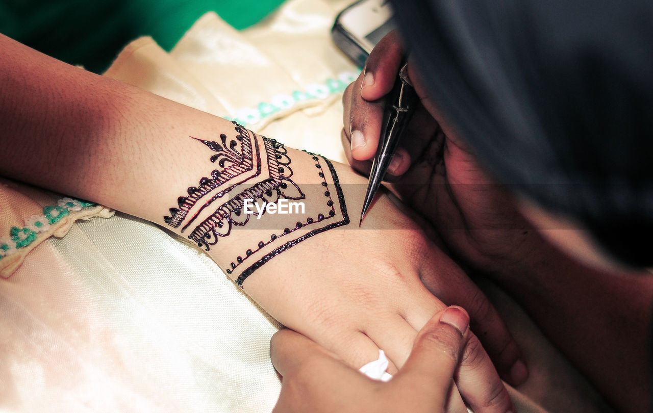 Cropped hand of woman getting henna tattoo