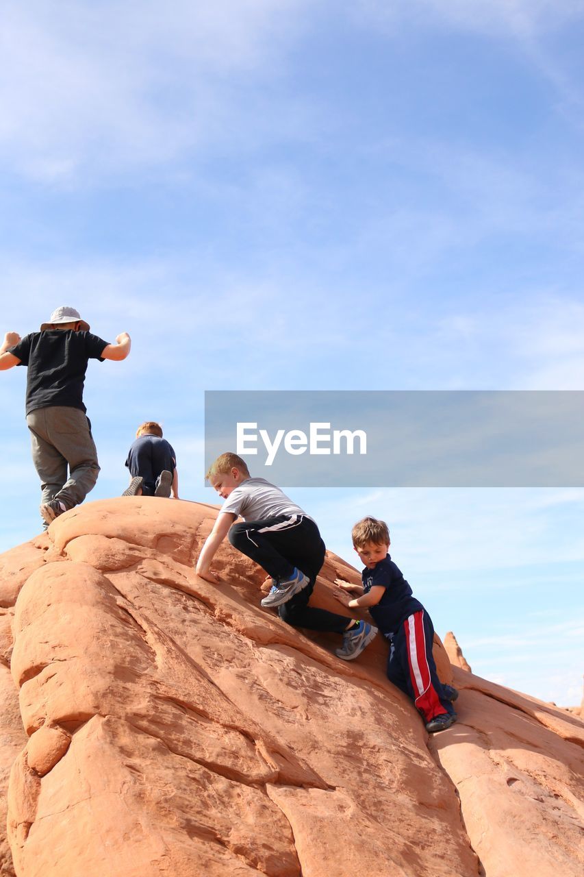 Low angle view of people on rock formation against sky