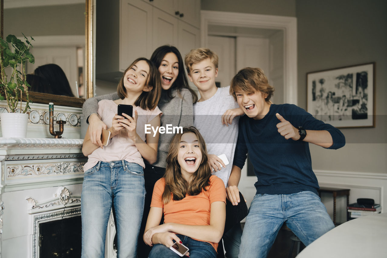 Portrait of cheerful friends with mobile phones in living room at home