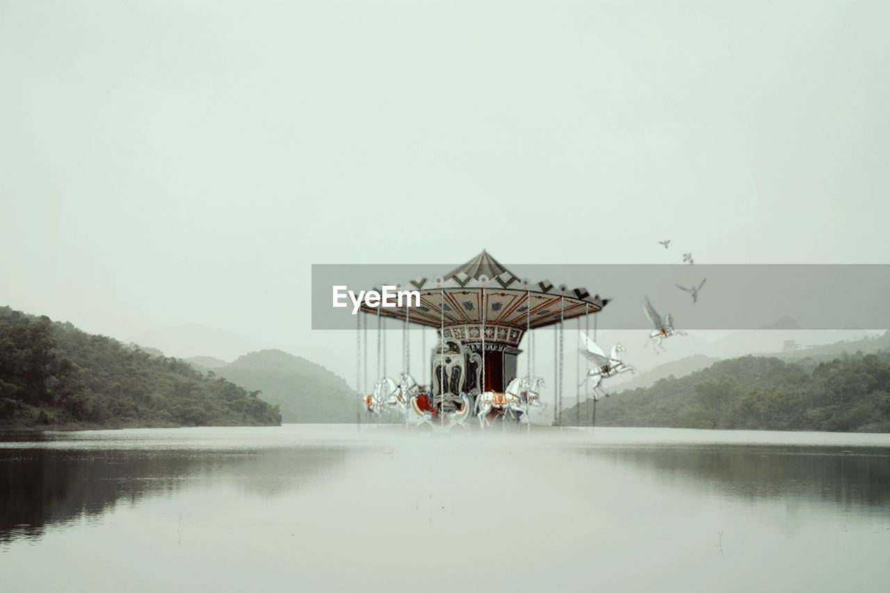 Digital composite of carousel horses flying over lake against clear sky