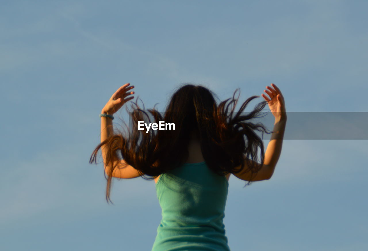 Rear view of young woman with tousled hair against sky