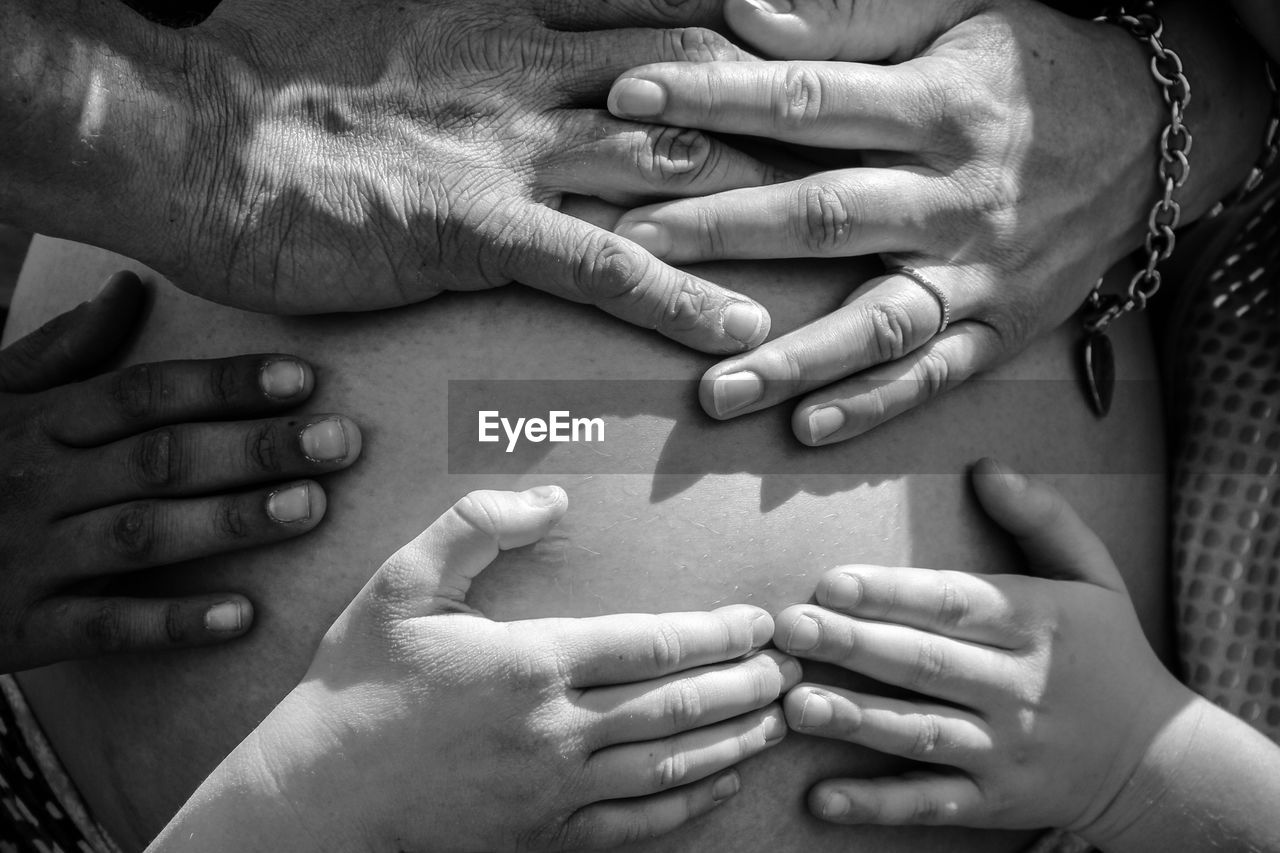Cropped hands of people touching pregnant woman belly