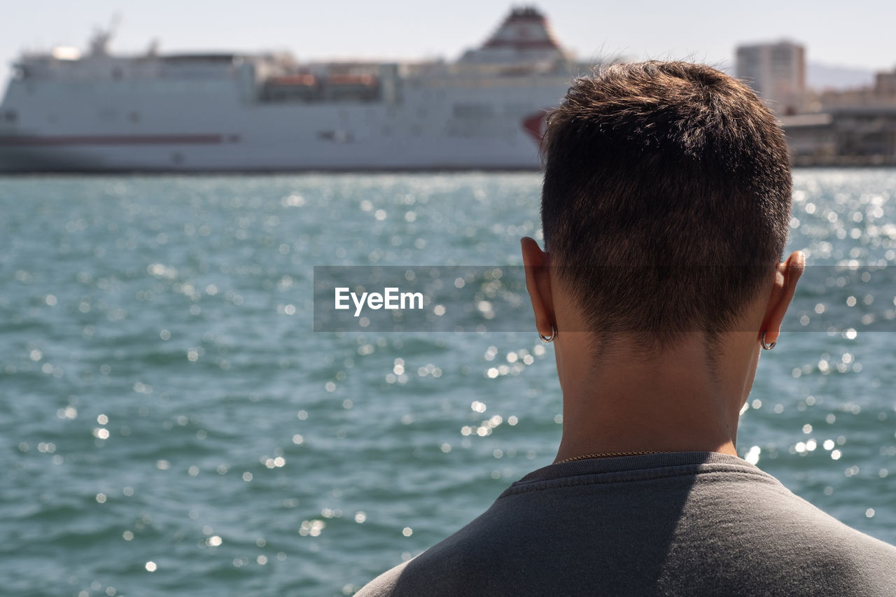 REAR VIEW OF MAN LOOKING AT SEA AGAINST BLURRED BACKGROUND