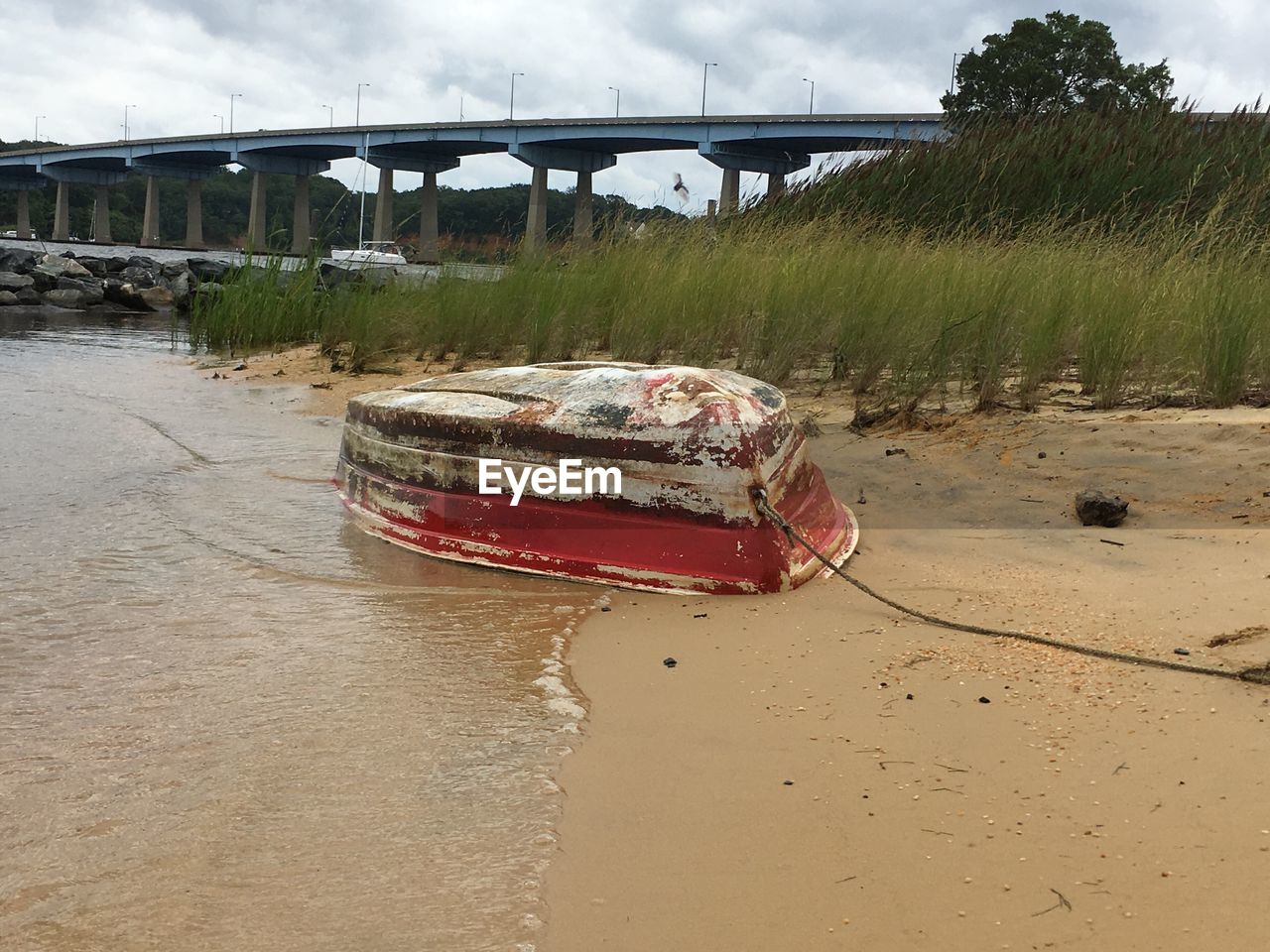 Overturned boat moored on river beach near bridge