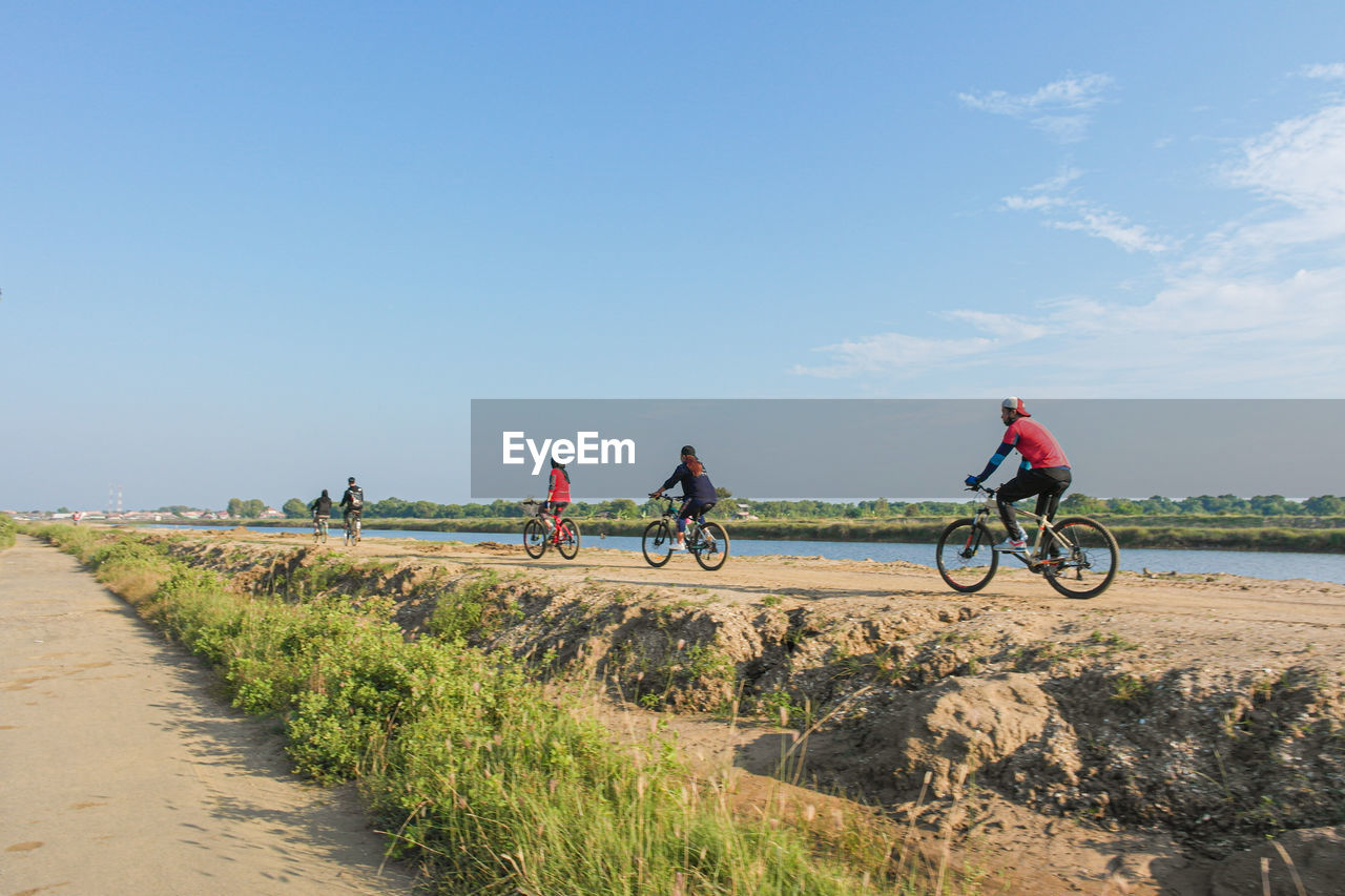 People riding bicycle on road against sky