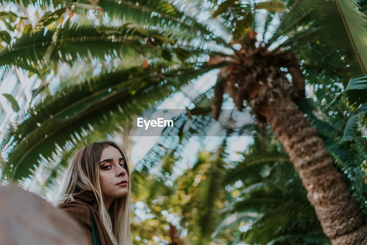 Portrait of young woman standing by palm tree