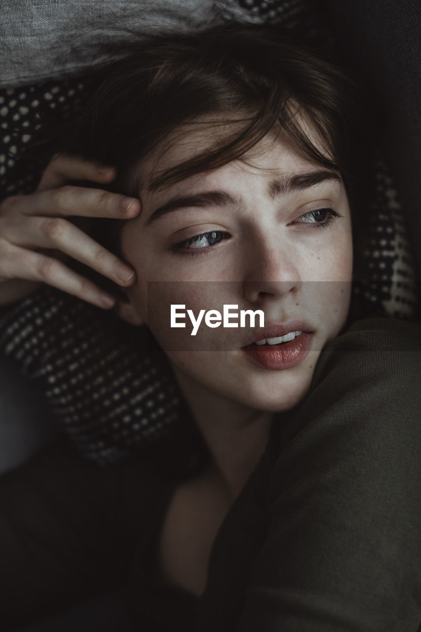 Worried woman looking away while lying on sofa