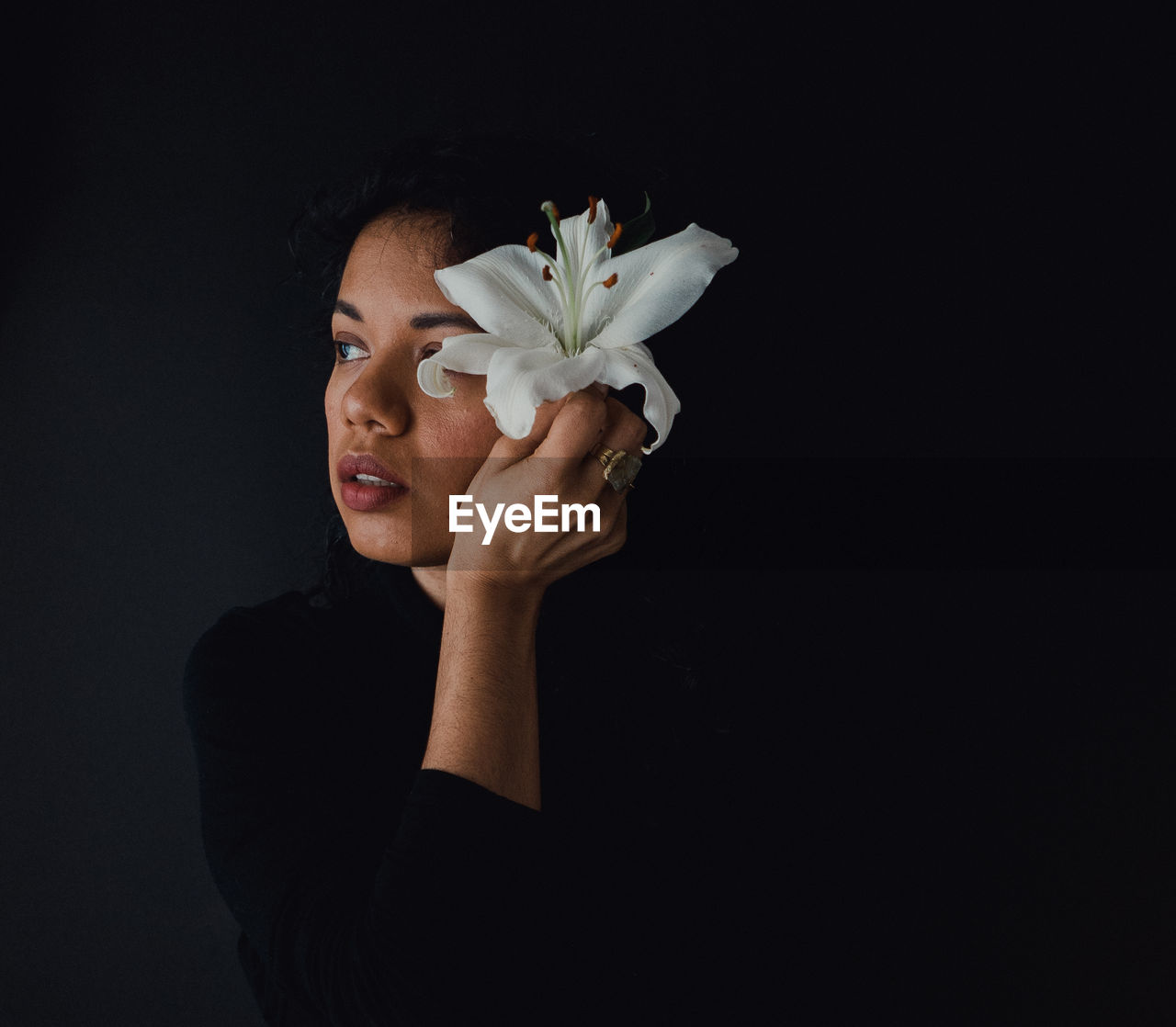 Thoughtful woman wearing flower against black background