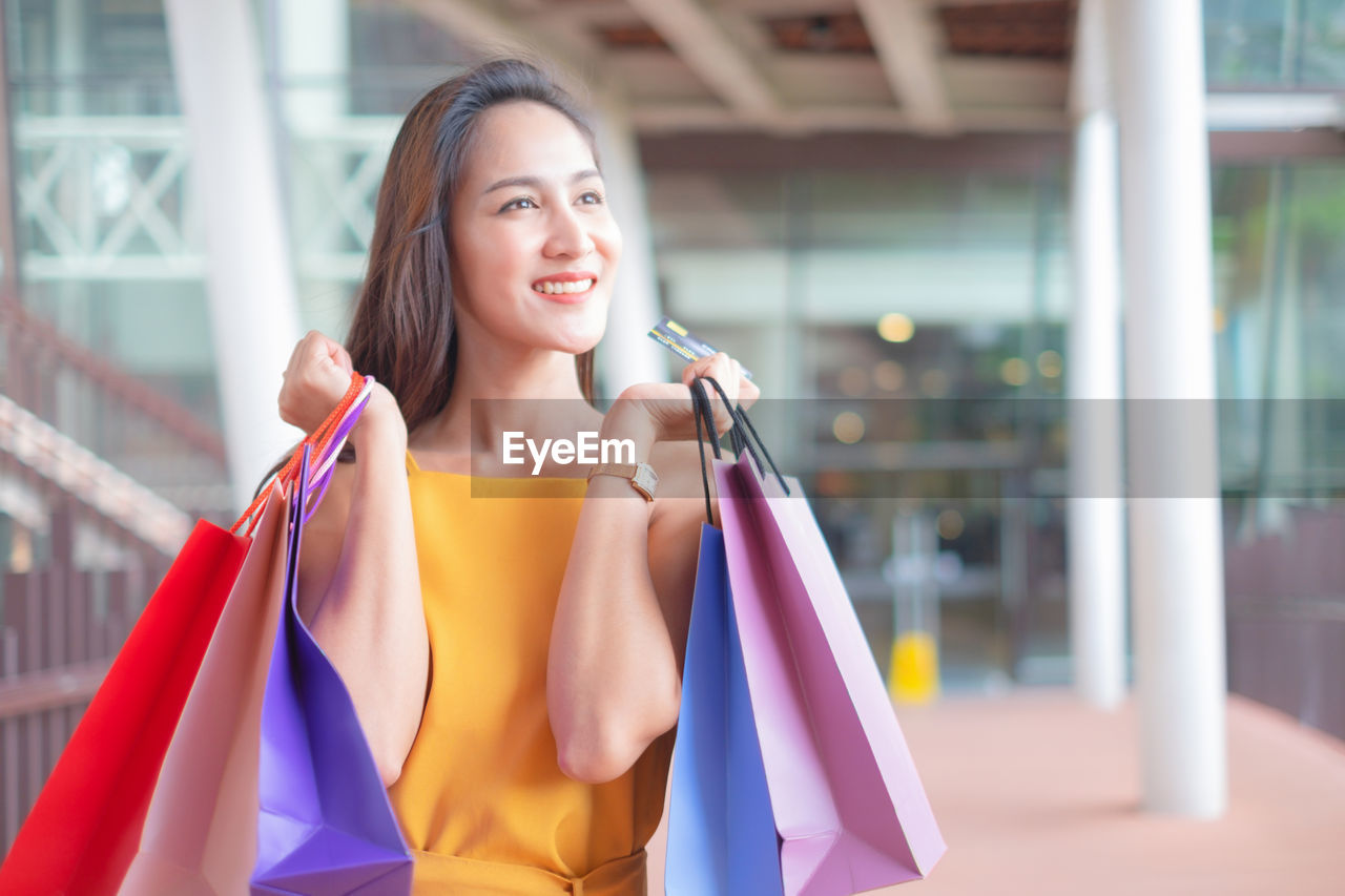 Smiling young woman with bags standing in shopping mall