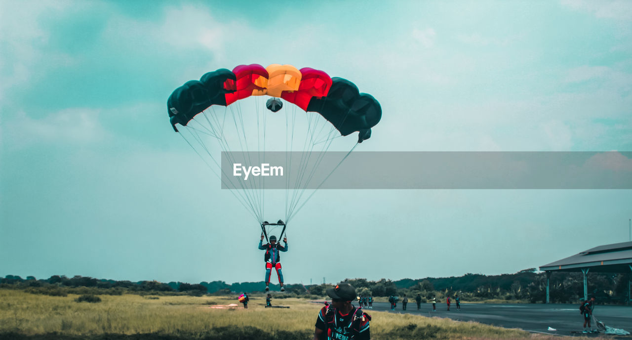 PEOPLE PARAGLIDING OVER FIELD