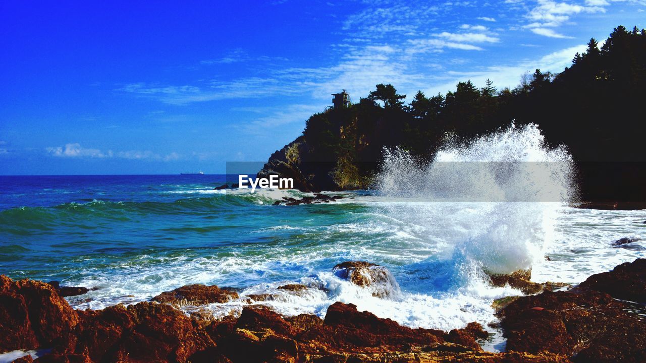 SCENIC VIEW OF SEA WAVES SPLASHING ON SHORE AGAINST SKY