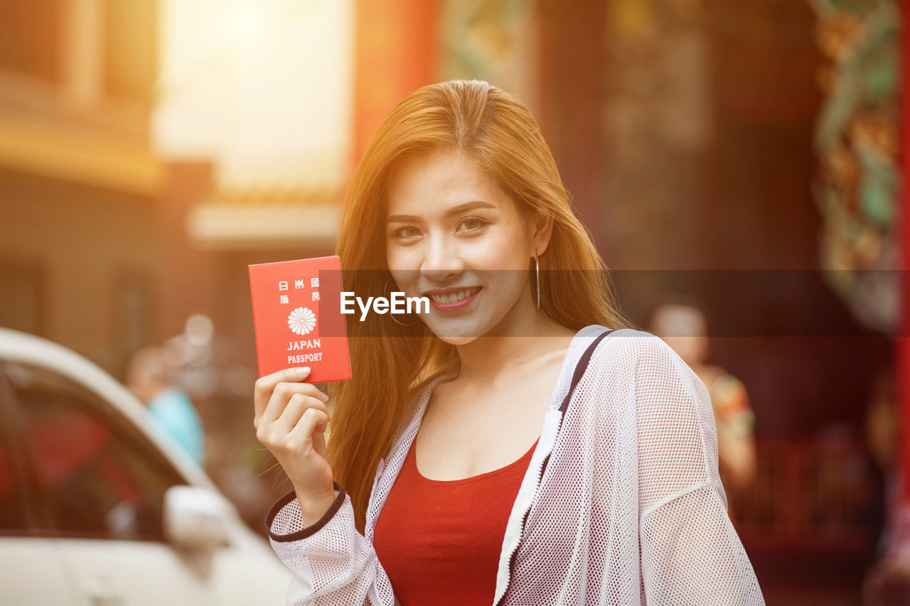 Portrait of smiling beautiful woman with japanese passport in city 