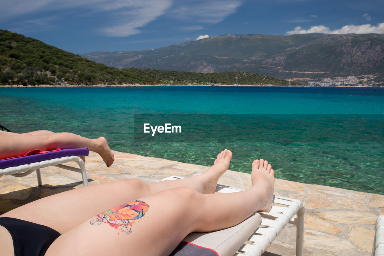 Young woman with tattoo sunbathing on sunbed by sea