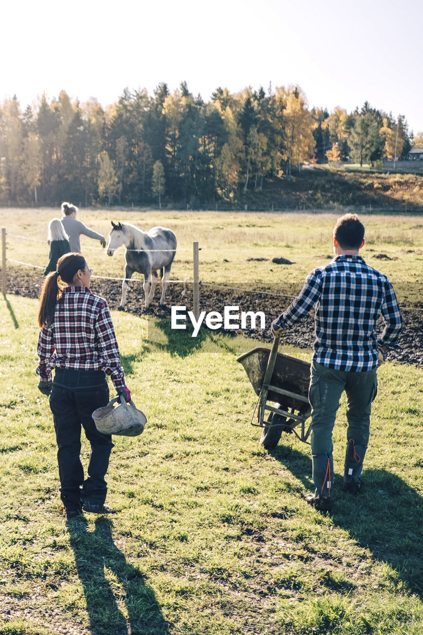 Multi-ethnic male and female farmers with equipment walking on field